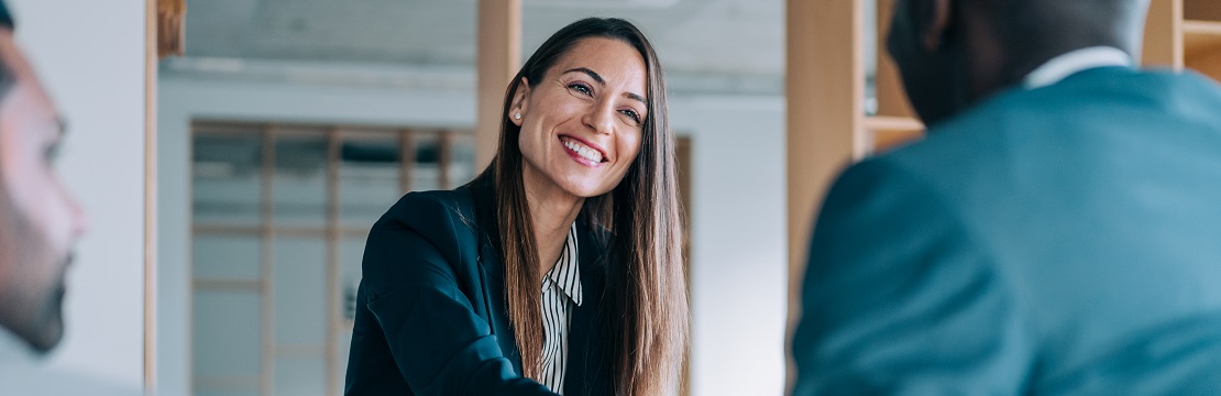 A professional woman shakes hands with another business man in an office setting.