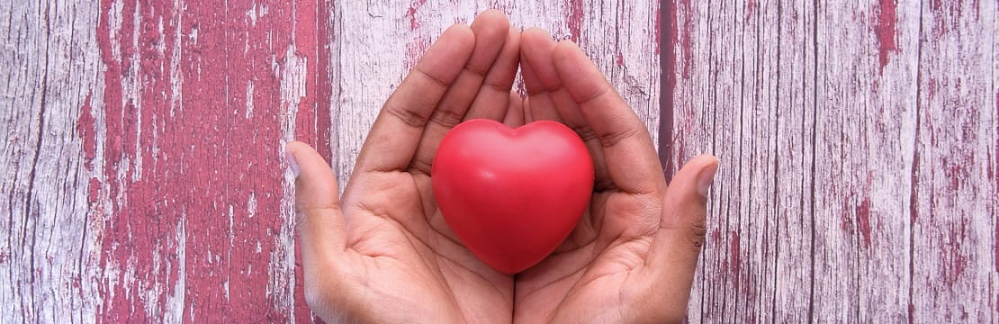 A close-up photo of two hands holding a red heart-shaped object